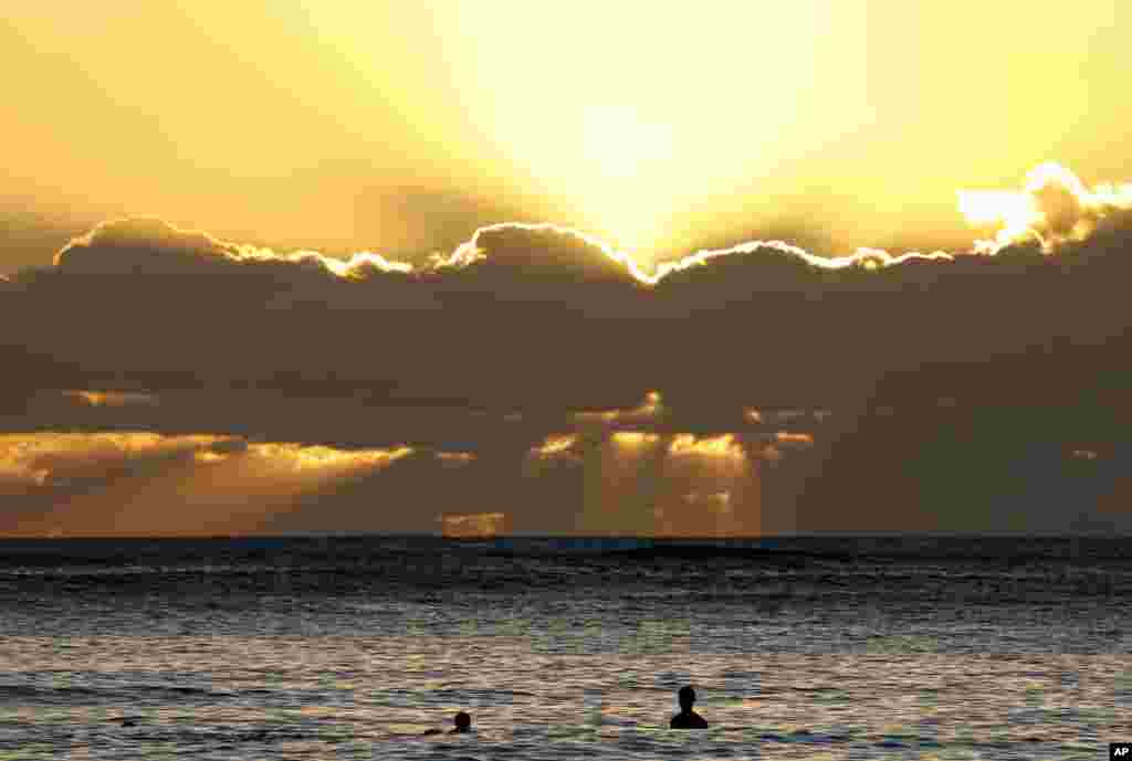 Swimmers watch the sunset behind clouds over the Pacific Ocean seen from Waikiki Beach in Honolulu, Hawaii, Dec. 31, 2016, the last sunset of 2016.