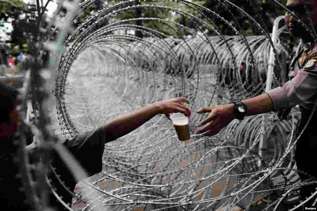 An Indonesian policeman buys a drink as he stands guard near the barbwire outside a court at the blasphemy trial of Jakarta's incumbent governor Basuki Tjahaja Purnama, also known as Ahok, in Jakarta, Indonesia.