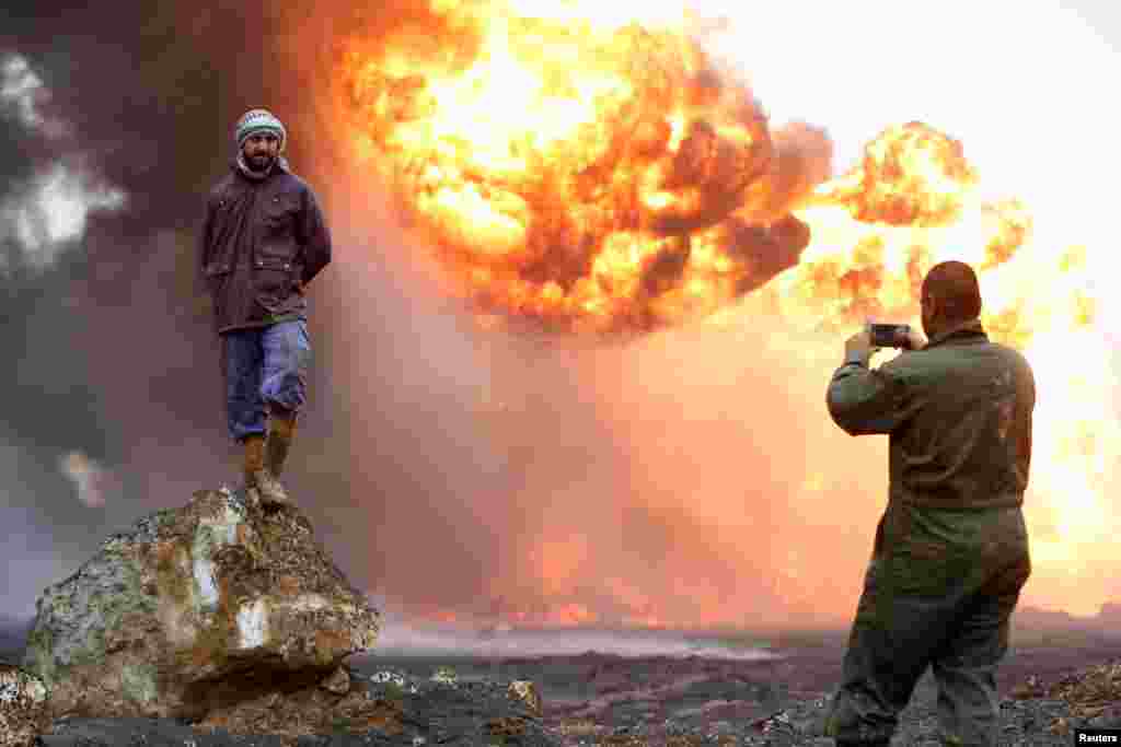 A man takes a photograph of his friend as thick smoke rises from a fire, which broke out at oil wells set ablaze by Islamic State militants before they fled the oil-producing region of Qayyara, Iraq, Jan. 28, 2017.