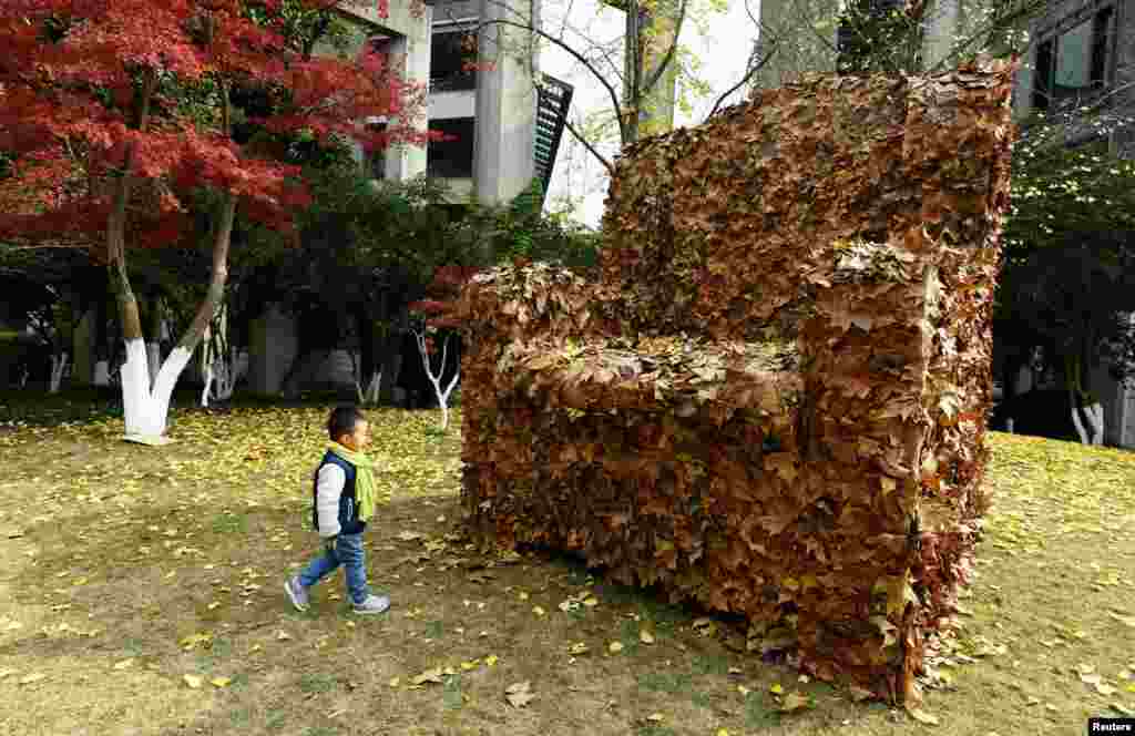 A child walks to an installation made from fallen leaves by college students, in the shape of an armchair, to help focus people's attention on the environment, in Hangzhou, Zhejiang province, China.
