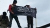FILE - Rebels from al-Qaida-affiliated Jabhat al-Nusra, also known as the Nusra Front, wave their brigade flag, as they step on the top of a Syrian air force helicopter at Taftanaz air base, Jan. 11, 2013.