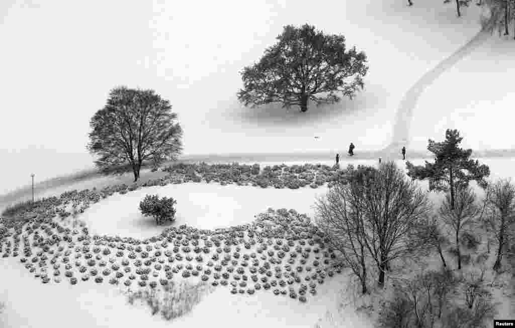 People stroll through the Olympic park during snowfall in Munich, Germany.