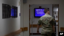 FILE - A member of the U.S. Army walks down the hall toward a monitor displaying COVID-19 safety information in Fort Meade, Md., March 25, 2020.