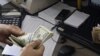 A currency exchange bureau worker counts US dollars, as Iranian bank notes are seen at right with portrait of late revolutionary founder Ayatollah Khomeini, in downtown Tehran, December 21, 2011. 