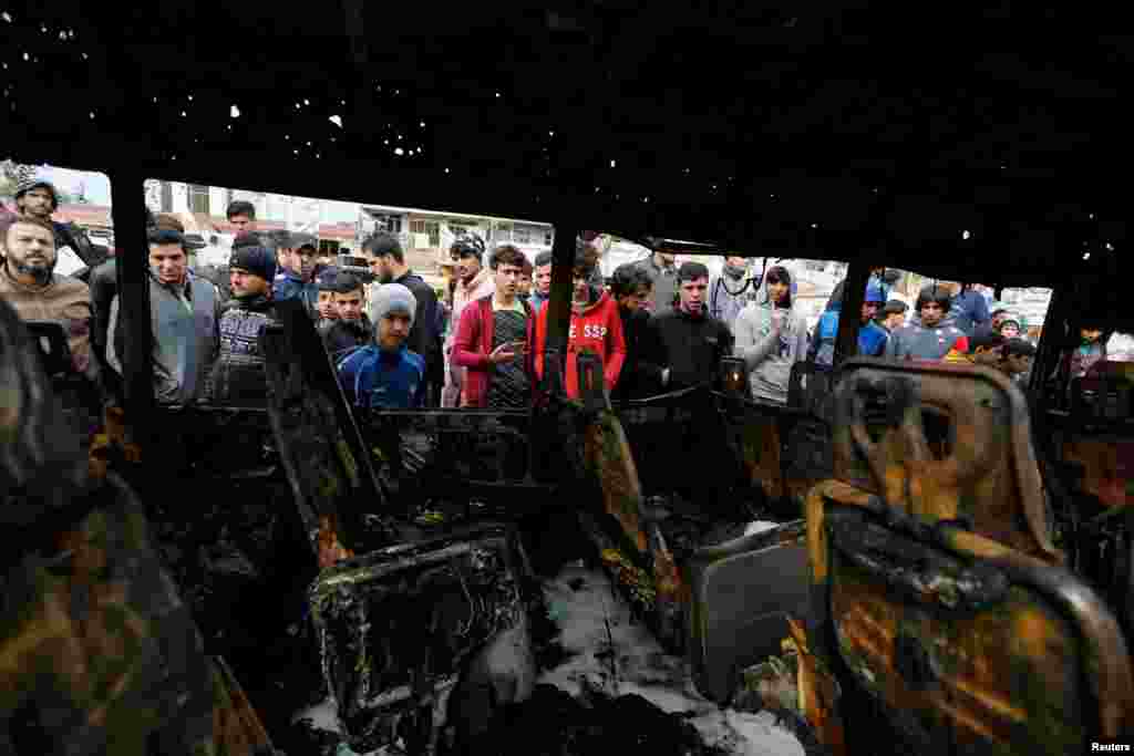 People look at a burned vehicle at the site of car bomb attack in a busy square at Baghdad's sprawling Sadr City district, Iraq.
