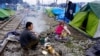 Refugee family attempts to stay warm along Macedonia-bound railroad tracks, Idomeni, Greece, March 16, 2016. (J. Dettmer/VOA)