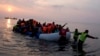 FILE - Volunteers help migrants and refugees on a dingy as they arrive at the shore of the northeastern Greek island of Lesbos, after crossing the Aegean sea from Turkey, March 20, 2016. 