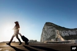 FILE- A woman walks on the Spanish side of the border between Spain and the British overseas territory of Gibraltar with the Rock of Gibraltar in the background, in La Linea de la Concepcion, Spain, March 1, 2017.