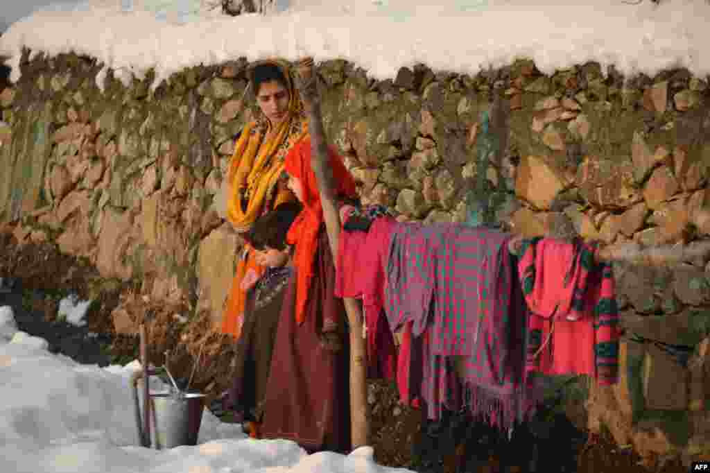 A Kashmiri woman waits as she fills water in an iron bucket on the outskirts of , India, following the season's first snowfall.