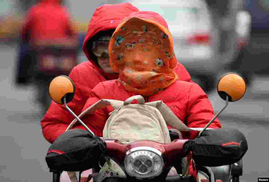 A woman covered her face with a scarf drives along a road on a winter day in Beijing, China.