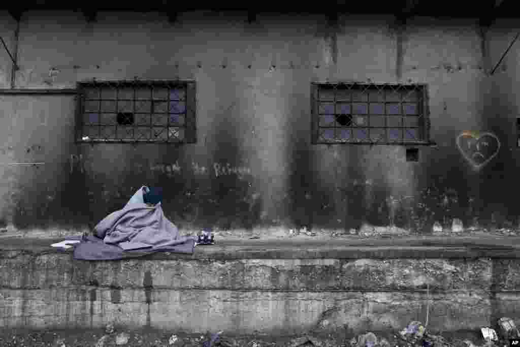 An Afghan refugee man wraps himself with a blanket to shield from the morning cold while sitting outside an abandoned warehouse where he and other refugees took refuge in Belgrade, Serbia, Monday, Feb. 6, 2017.