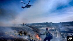 Para pemadam kebakaran memangkas semak-semak di bukit dekat pusat perbelanjaan Mission Valley Shopping Mall di San Diego, Selasa, 21 Januari 2025. (Foto: Gregory Bull/AP Photo)