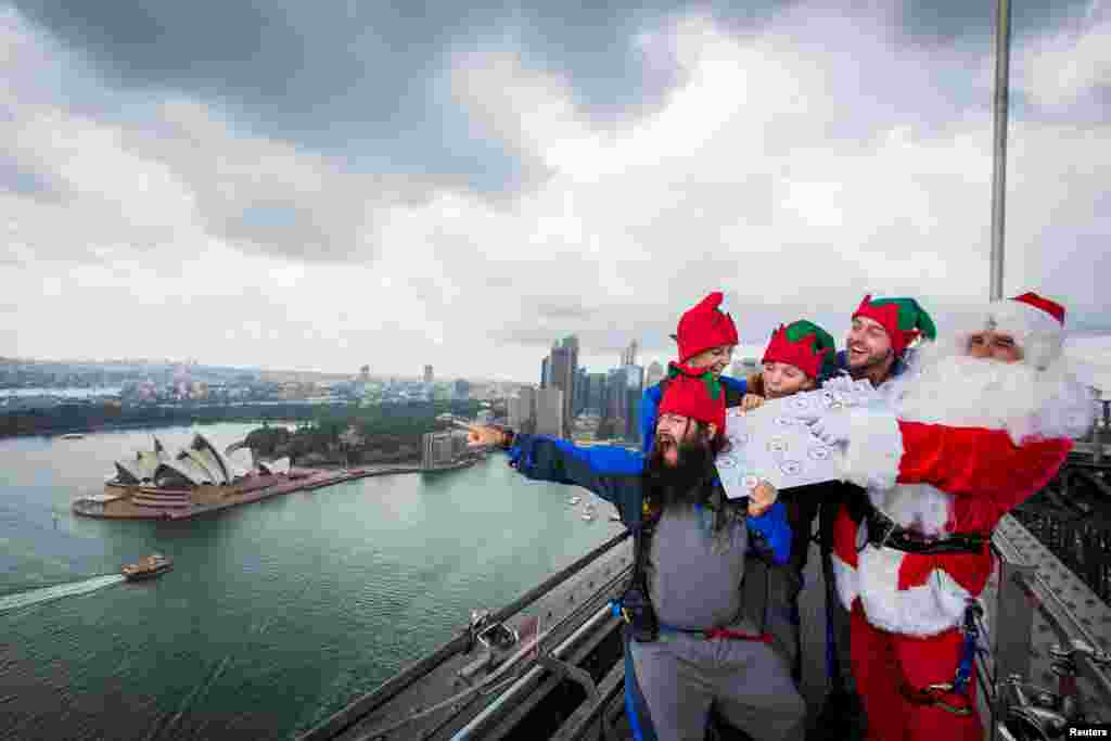People dressed as Santa Claus and his elves stand on top of the Sydney Harbour Bridge with a map featuring Australian homes at which to deliver gifts on Christmas day.