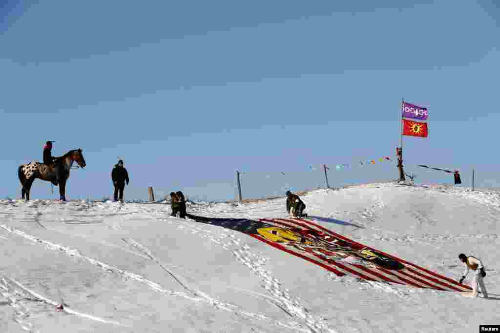 A young Native American man on horseback watches veterans unfurl a flag near the Oceti Sakowin camp as "water protectors" continue to demonstrate against plans to run the Dakota Access pipeline near the Standing Rock Indian Reservation, near Cannon Ball, North Dakota, Dec. 4, 2016.