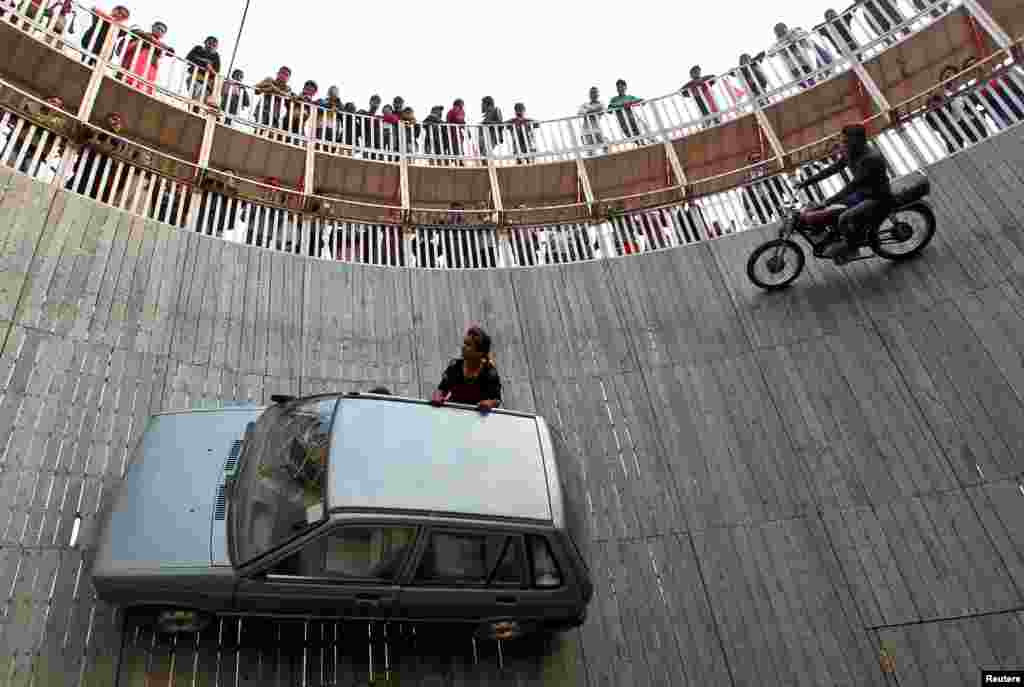 Stunt performers ride a motorcycle and a car on the walls of the "Well of Death" at the Magh Mela fair in Allahabad, India.