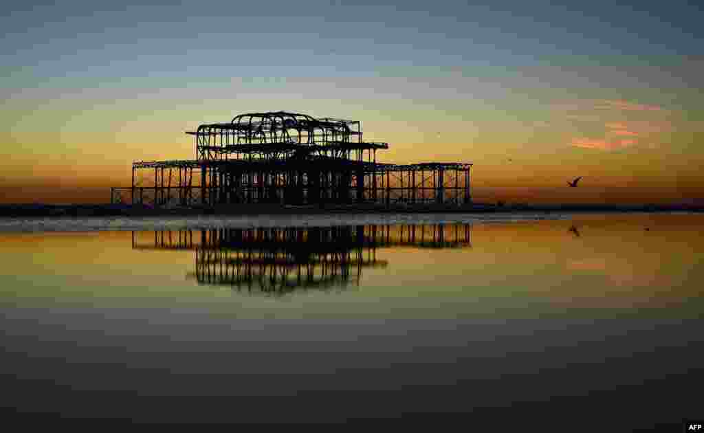 A mumuration of Starlings flock to the remains of the West Pier near Brighton beach, as the sun sets on the horizon in Brighton, southern England.