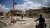 FILE - A man rides on a motorbike as another one walks past damaged buildings in the rebel-controlled area of al-Nashabyia town in Eastern Ghouta, Syria, April 13, 2016. 