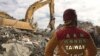 FILE - A member of rescue teams stands by as heavy excavation machinery continues to dig through the rubble of a collapsed building complex in Tainan, Taiwan, Thursday, Feb. 11, 2016.