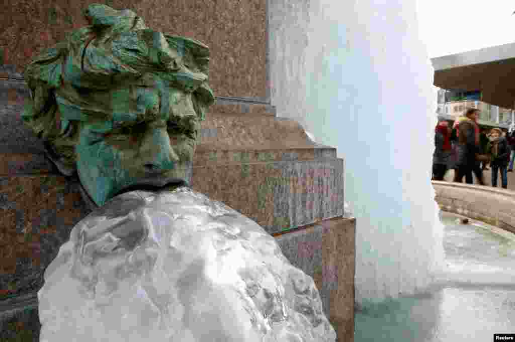 People walk past a frozen public fountain during cold winter weather in Zurich, Switzerland.