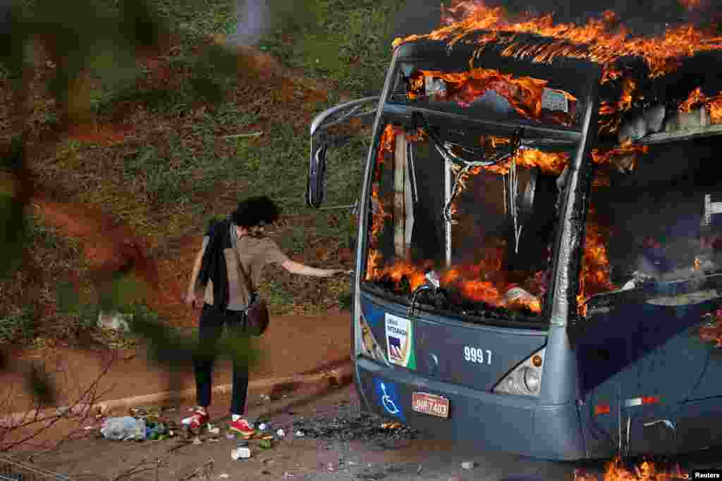 A man lights up his cigarette with the flames of a bus burned by anti-government demonstrators during a protest against the constitutional amendment PEC 55, which limits public spending, in front of Brazil's National Congress in Brasilia, Dec. 13, 2016.