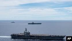 FILE - In this photo provided by U.S. Navy, the USS Ronald Reagan (CVN 76, front) and USS Nimitz (CVN 68, rear) Carrier Strike Groups sail together in formation, in the South China Sea, July 6, 2020.
